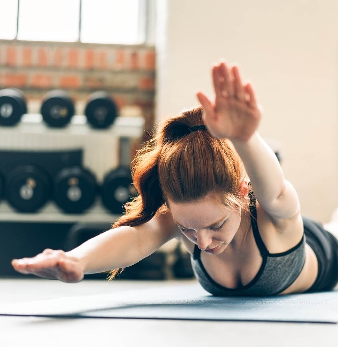 Vrouw met rood haar doet een oefening op een yogamat in een fitnessruimte.