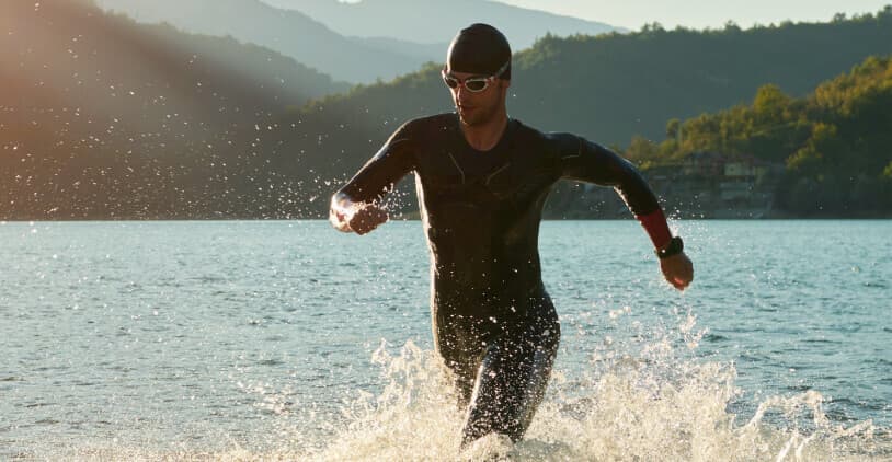 Man in wetsuit en zwembril rent uit het water tijdens een triatlon.