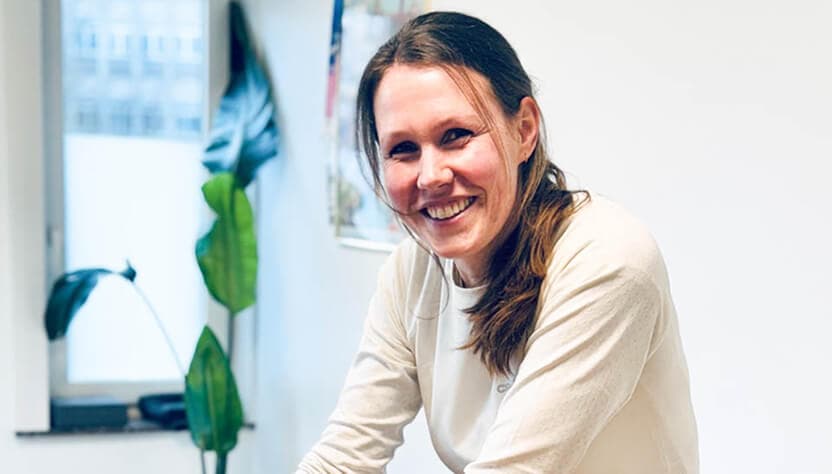 Portret van een glimlachende vrouw met een witte trui in een kantooromgeving.